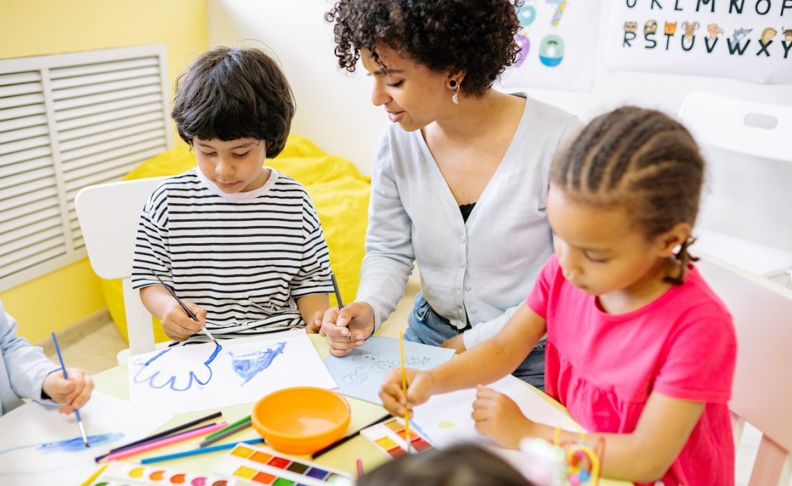 two young students painting with their school teacher